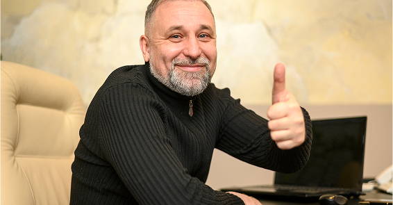 Confident professional advisor giving thumbs up with laptop nearby